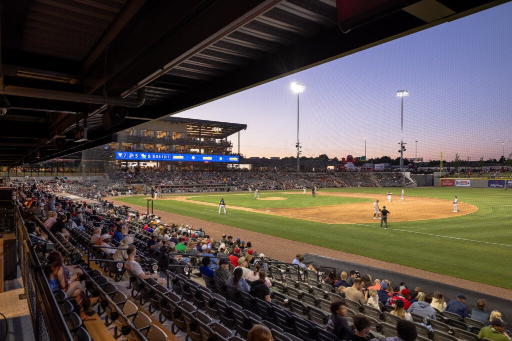 Erlanger Park - Chattanooga Lookouts - Packed baseball stadium at twilight with fans in dark bleachers, field lit by tall stadium lights, modern press box visible above home plate