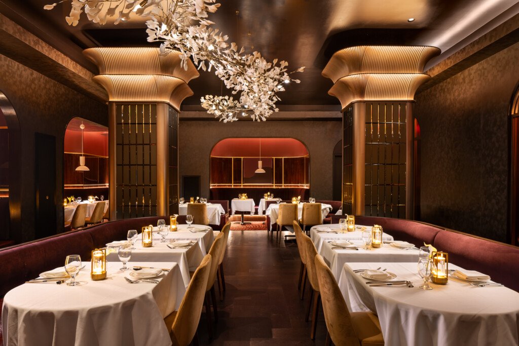 Philippe Chow - Nashville - Fine dining room with white-draped tables, sculptural brass columns, ornate crystal chandelier, and warm ambient lighting throughout the elegant space