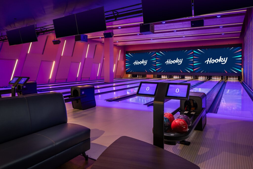 Hooky, Nashville Yards - Interior of a contemporary bowling facility featuring purple and magenta neon lighting, multiple lanes with scoring screens, red bowling balls, and a lounge area with dark seating.