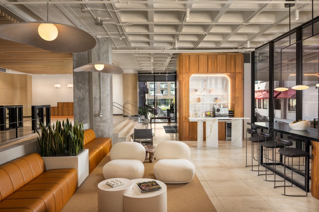 Open commercial space with coffered ceiling, orange leather seating, cream poufs, wood accent wall with illuminated display, and bar seating area