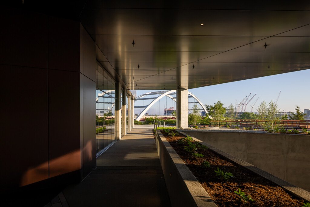 Covered terrace with concrete planter beds, steel columns, and floor-to-ceiling windows framing contemporary architecture beyond