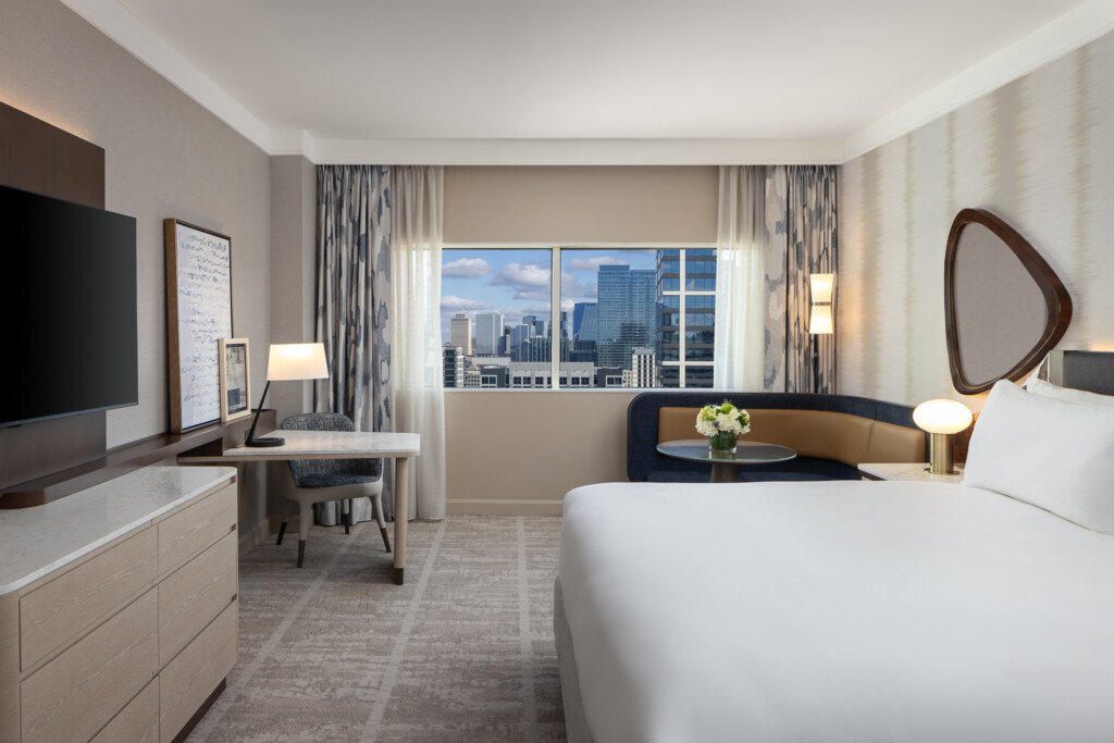 Loews Vanderbilt - Spacious hotel room with king bed, work desk, flat-screen TV, and floor-to-ceiling windows overlooking a city skyline