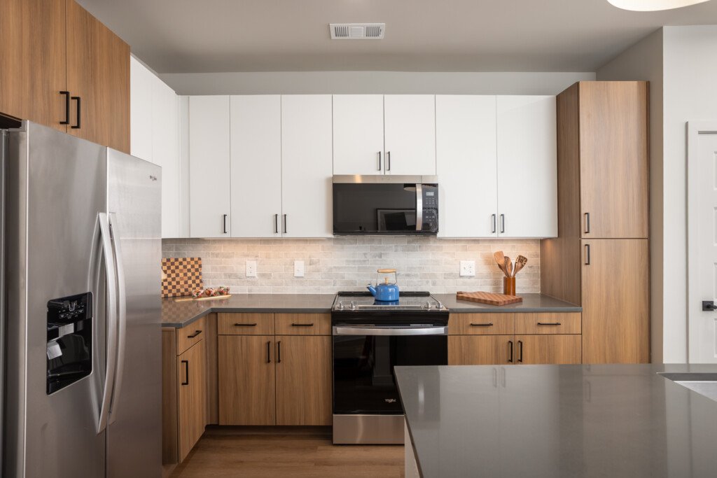 Contemporary kitchen with warm wood lower cabinets and white upper cabinets, stainless steel appliances, subway tile backsplash, and gray countertops.