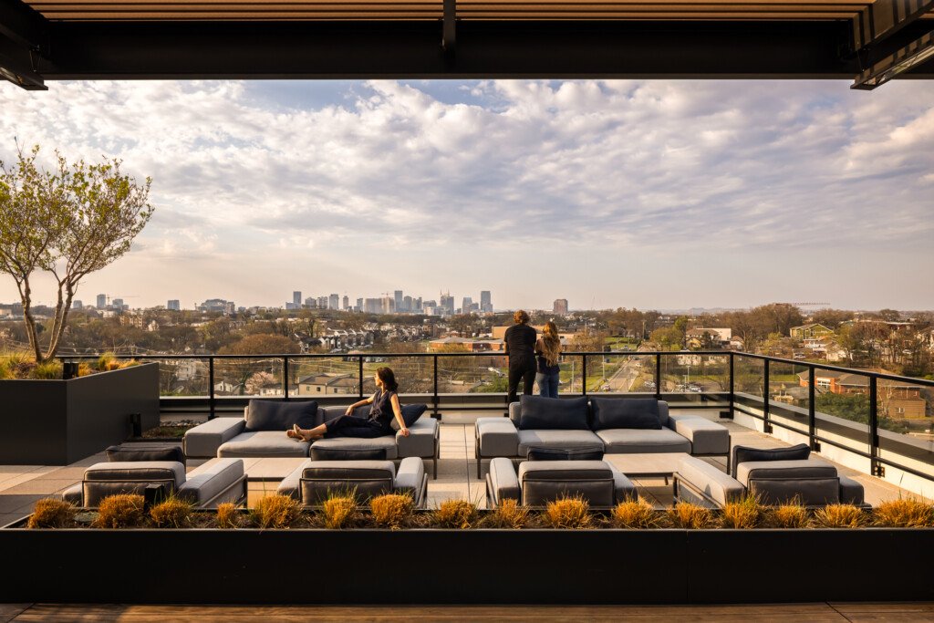 445 Park Commons - GEODIS - Rooftop terrace with gray modular seating, ornamental grasses, and metal railing overlooking a distant cityscape under cloudy skies